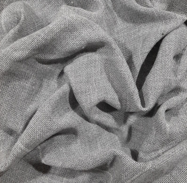 May include: Close-up of a gray, textured fabric with a woven pattern. The fabric is wrinkled and folded, creating a soft, drapey look.