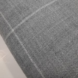 May include: Close-up of gray fabric with a woven texture. White lines form a grid pattern across the material. The fabric appears to be folded over, revealing the texture and weave of the material.