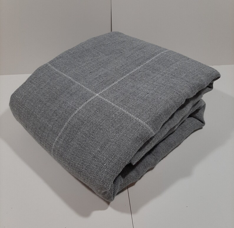 May include: Folded gray blanket with a white grid pattern. The blanket is made of a textured fabric and is neatly folded, showcasing its clean lines and simple design. The blanket is a neutral color, suitable for various home decor styles.