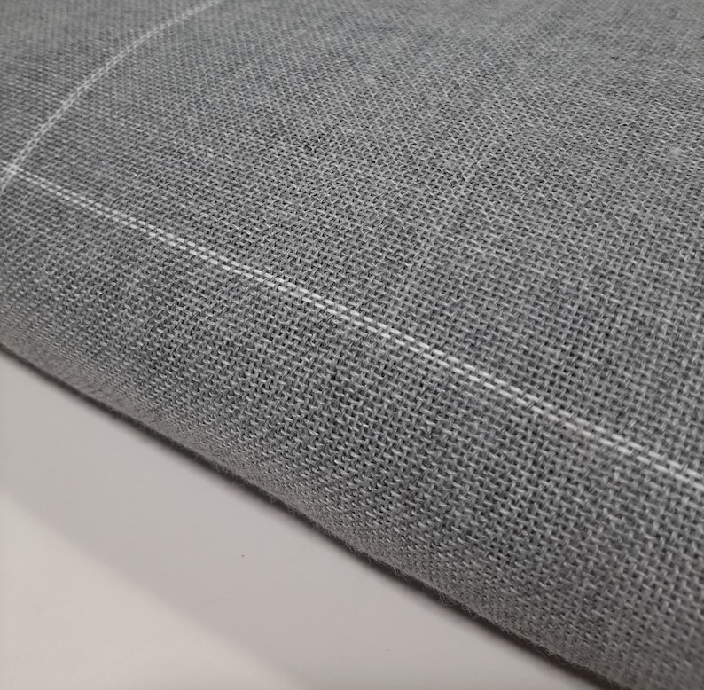 May include: Close-up of a gray fabric with a woven texture. The fabric has a subtle white grid pattern running across it. The material appears to be soft and could be used for clothing or home decor.