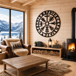 Op de afbeelding: Een gezellige woonkamer met een houten salontafel, een leren fauteuil met een schapenvacht en een decoratief kussen met een bosontwerp. Een zwarte open haard en een groot zwart kunstwerk aan de muur dragen bij aan de rustieke charme. Een raam biedt uitzicht op bergen en een meer.
