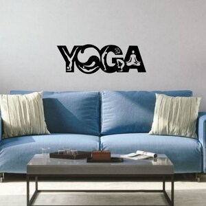 Puede incluir: Un adhesivo de pared negro con la palabra YOGA en letras may&uacute;sculas grandes. Las letras est&aacute;n estilizadas con siluetas de personas realizando varias posturas de yoga, incluyendo una figura en meditaci&oacute;n sentada y el s&iacute;mbolo Om integrado.