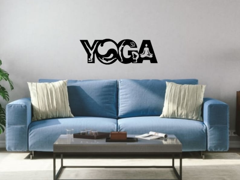 Puede incluir: Un adhesivo de pared negro con la palabra YOGA en letras may&uacute;sculas grandes. Las letras est&aacute;n estilizadas con siluetas de personas realizando varias posturas de yoga, incluyendo una figura en meditaci&oacute;n sentada y el s&iacute;mbolo Om integrado.