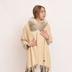May include: A beige shawl with a fox fur collar. The shawl has a fringe trim and is made of a soft, warm fabric.