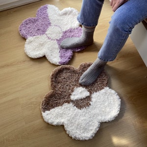May include: Two fluffy flower-shaped bath mats in purple and white and brown and white.