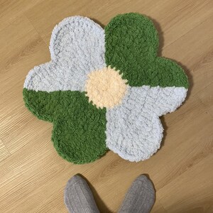 May include: A fluffy, green and blue flower-shaped rug with a light yellow center. The rug is made of soft, textured yarn.