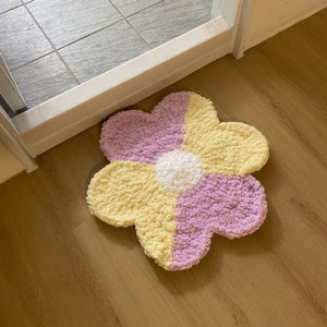 May include: A fluffy, yellow and purple flower-shaped rug with a white center. The rug is made of soft, plush material and is perfect for adding a touch of whimsy to any room.