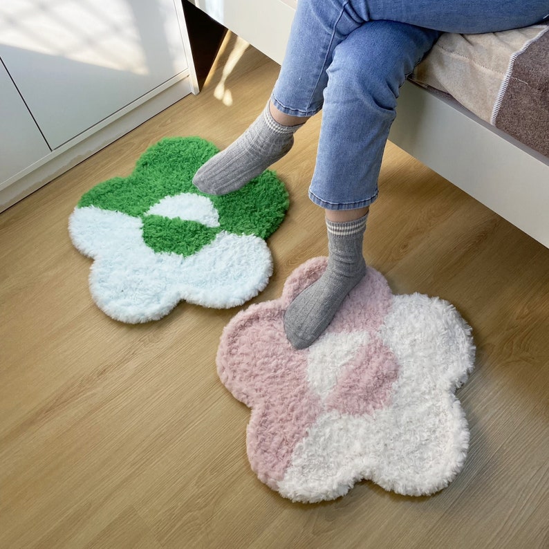 May include: Two fluffy flower-shaped rugs in pink, white, and green. The rugs are on a wooden floor.