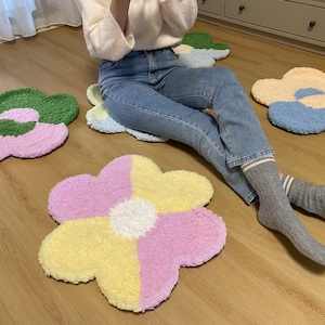 May include: Four fluffy flower-shaped rugs in different colors: green, pink, blue, and yellow. The rugs are arranged on a wooden floor.