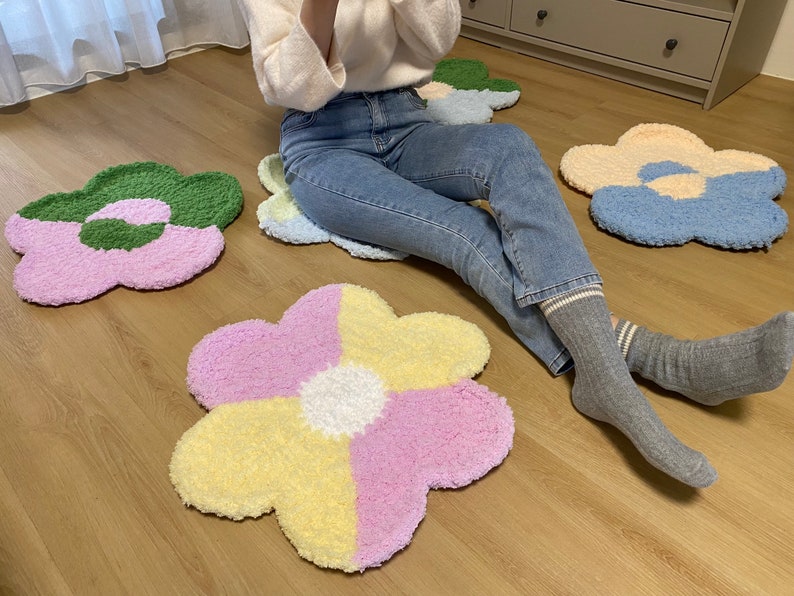 May include: Four fluffy flower-shaped rugs in different colors: green, pink, blue, and yellow. The rugs are arranged on a wooden floor.