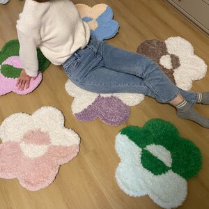 May include: Five colorful flower-shaped rugs in shades of pink, green, white, purple, and brown. The rugs are made of fluffy, soft material and are arranged on a wooden floor.