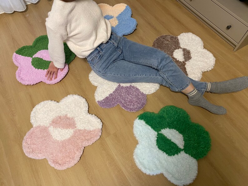May include: Five colorful flower-shaped rugs in shades of pink, green, white, purple, and brown. The rugs are made of fluffy, soft material and are arranged on a wooden floor.