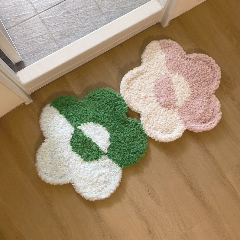 May include: Two fluffy flower-shaped rugs, one green and white, the other pink and white, on a wooden floor.