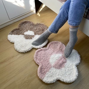 May include: Two fluffy, flower-shaped rugs in brown and pink with white centers. The rugs are on a wooden floor.