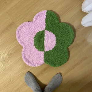 May include: A pink and green flower-shaped rug with a fluffy texture. The rug is on a wooden floor.