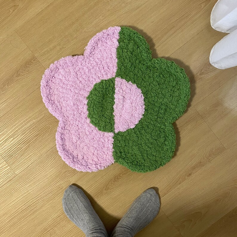 May include: A pink and green flower-shaped rug with a fluffy texture. The rug is on a wooden floor.