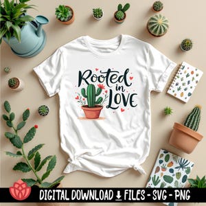 May include: White t-shirt featuring a green cactus graphic and the text "Rooted in Love". The cactus is in a brown pot and has red flowers. There are pink hearts around the text.