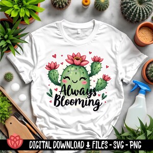 May include: White t-shirt featuring a green cactus illustration with a smiling face and pink flowers. The text "Always Blooming" is printed on the shirt.