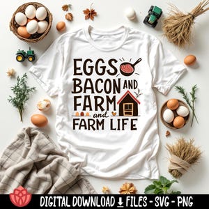 May include: White t-shirt with the text "EGGS BACON AND FARM and FARM LIFE" in a bold, rustic font. The design includes illustrations of a frying pan with bacon, a small house, and eggs. The shirt is surrounded by eggs, hay, and toy tractors.