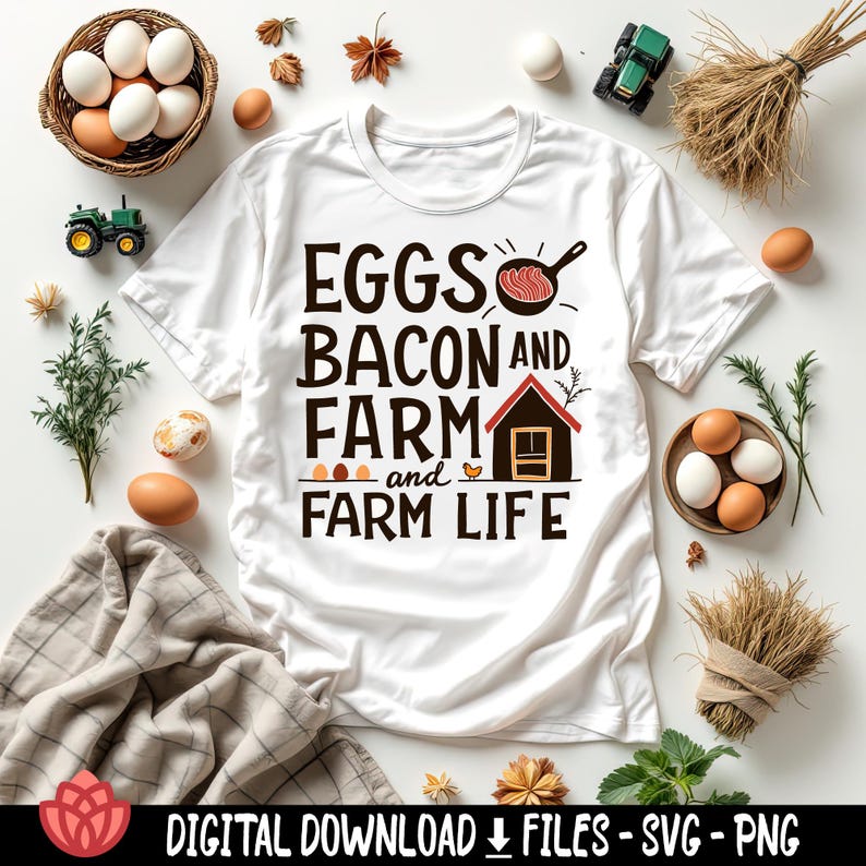 May include: White t-shirt with the text "EGGS BACON AND FARM and FARM LIFE" in a bold, rustic font. The design includes illustrations of a frying pan with bacon, a small house, and eggs. The shirt is surrounded by eggs, hay, and toy tractors.