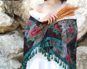 Könnte beinhalten: Ein schwarzer Spitzenschal mit roten und grünen Blumenstickereien und türkisfarbenen Quasten. Der Schal ist über die Schultern einer Person gelegt und wird in der Hand gehalten.
