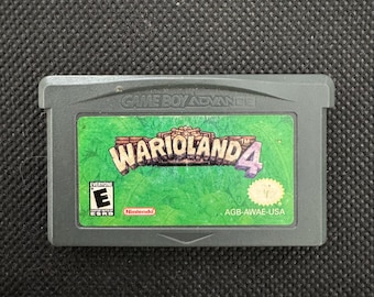 May include: A gray Game Boy Advance video game cartridge for Wario Land 4. The label features a green background with the game title in stylized lettering, an ESRB Everyone rating symbol, a Nintendo logo, and the product code AGB-AWAE-USA.