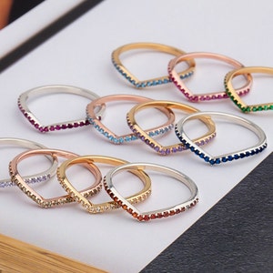 May include: A set of nine silver and gold rings with a V-shaped design. Each ring is adorned with a row of colourful gemstones.