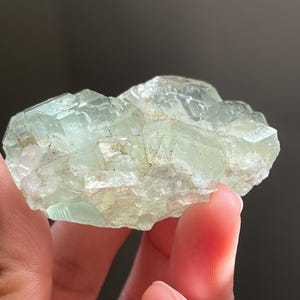 Puede incluir: Un racimo de cristales de fluorita transl&uacute;cidos de color verde p&aacute;lido con una estructura c&uacute;bica. El esp&eacute;cimen mineral presenta bordes geom&eacute;tricos afilados e inclusiones internas visibles, mostrando un tono verde menta claro en toda la formaci&oacute;n.