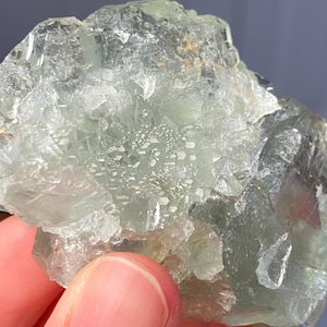 Puede incluir: Un racimo de cristales de fluorita verde p&aacute;lido, crudo y transl&uacute;cido, con facetas geom&eacute;tricas angulares y afiladas y una textura cristalina v&iacute;trea. El esp&eacute;cimen mineral muestra inclusiones internas y niveles variables de claridad en su estructura.