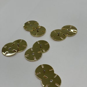 May include: Eight gold-coloured metal discs with a small metal pin in the centre of each disc. The discs have a decorative design of eight evenly spaced slots around the edge.