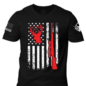 May include: Black t-shirt featuring a distressed American flag design. The flag incorporates a red deer silhouette and a rifle. The left sleeve displays a small American flag, and the right sleeve has a white hunting-themed graphic.