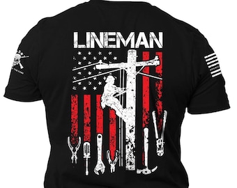 May include: Black t-shirt with a white graphic of a lineman working on a power line in front of an American flag with tools. The text "LINEMAN" is at the top of the graphic.
