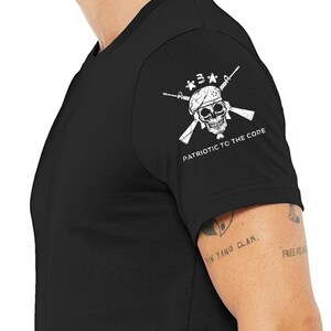 May include: Black t-shirt with a white skull and crossbones graphic on the right sleeve. The graphic includes three stars and the text "PATRIOTIC TO THE CORE".