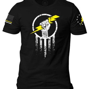 K&ouml;nnte beinhalten: Schwarzes T-Shirt mit einer wei&szlig;en und gelben Grafik einer Faust, die einen Blitz in einem Kreis h&auml;lt. Die Grafik ist auf eine wei&szlig;-schwarze amerikanische Flagge gelegt.
