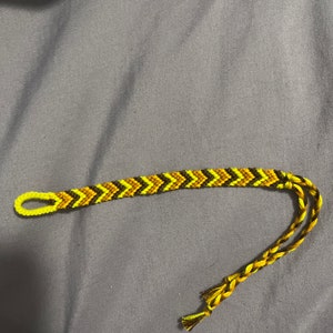 May include: A friendship bracelet with a chevron pattern in yellow, brown and black.