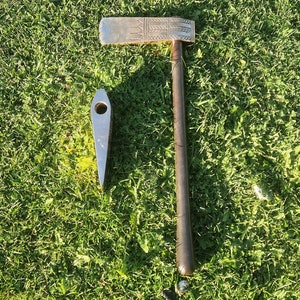 May include: Two metal tools, one with a wooden handle and a silver blade with a decorative pattern, and the other a silver blade with a pointed tip, on a green grassy surface.