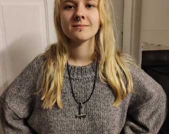 May include: A woman with long blonde hair wearing a gray knitted sweater with a black cord necklace and a silver pendant.