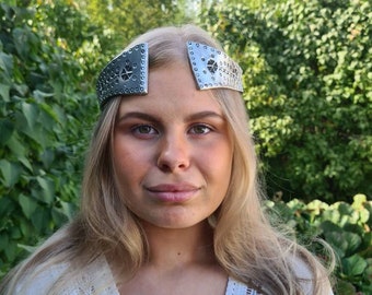 May include: A silver headband with a geometric design. The headband is worn by a person with long blonde hair.