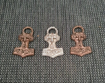 May include: Three silver and bronze Mjolnir pendants with intricate details. The pendants are in the shape of Thor's hammer, a symbol of strength and protection in Norse mythology.