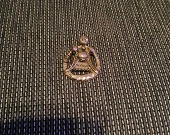 May include: A gold-toned metal charm in the shape of a woman holding a heart. The charm has intricate details and a delicate design.