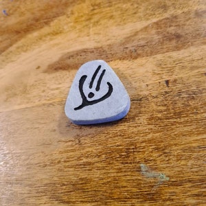 May include: A grey triangular stone with a black symbol on it. The symbol is a stylised design with three lines and a dot.