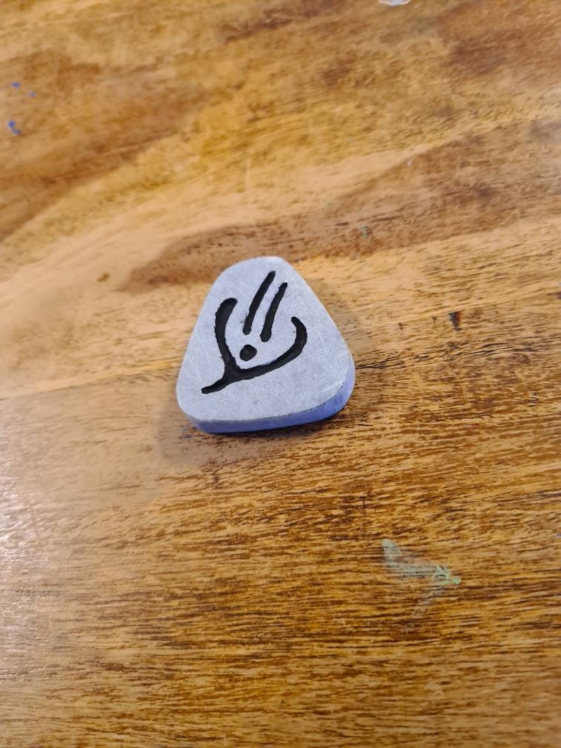 May include: A grey triangular stone with a black symbol on it. The symbol is a stylised design with three lines and a dot.