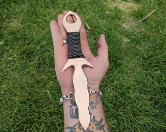 May include: A copper-colored dagger with a black leather wrap handle. The dagger has a unique, pointed blade with a small hole near the top.