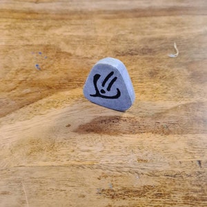 May include: A grey triangular stone with a black symbol on it. The symbol is a stylised hand with three fingers and a dot in the palm.