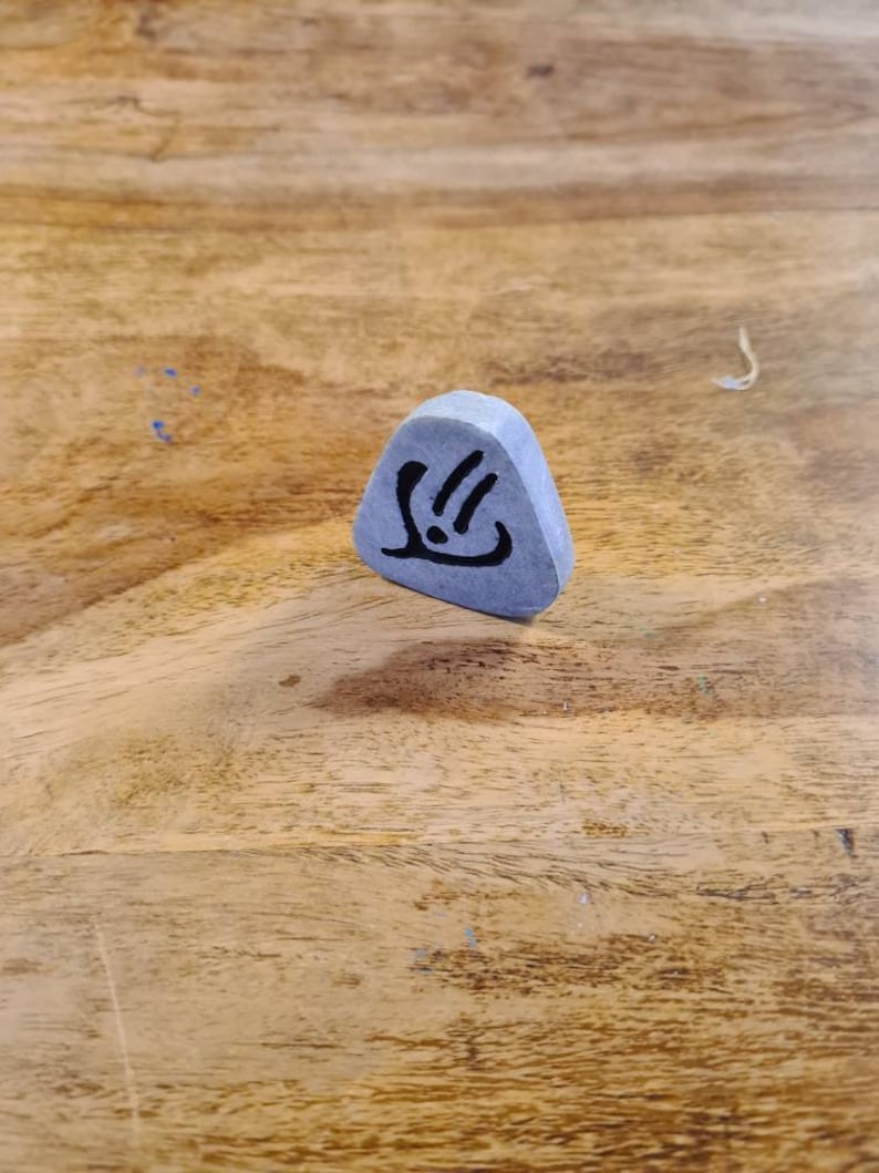 May include: A grey triangular stone with a black symbol on it. The symbol is a stylised hand with three fingers and a dot in the palm.