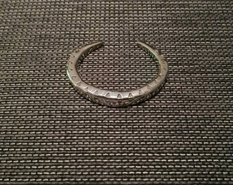May include: A silver bangle bracelet with a decorative design of triangles and circles.