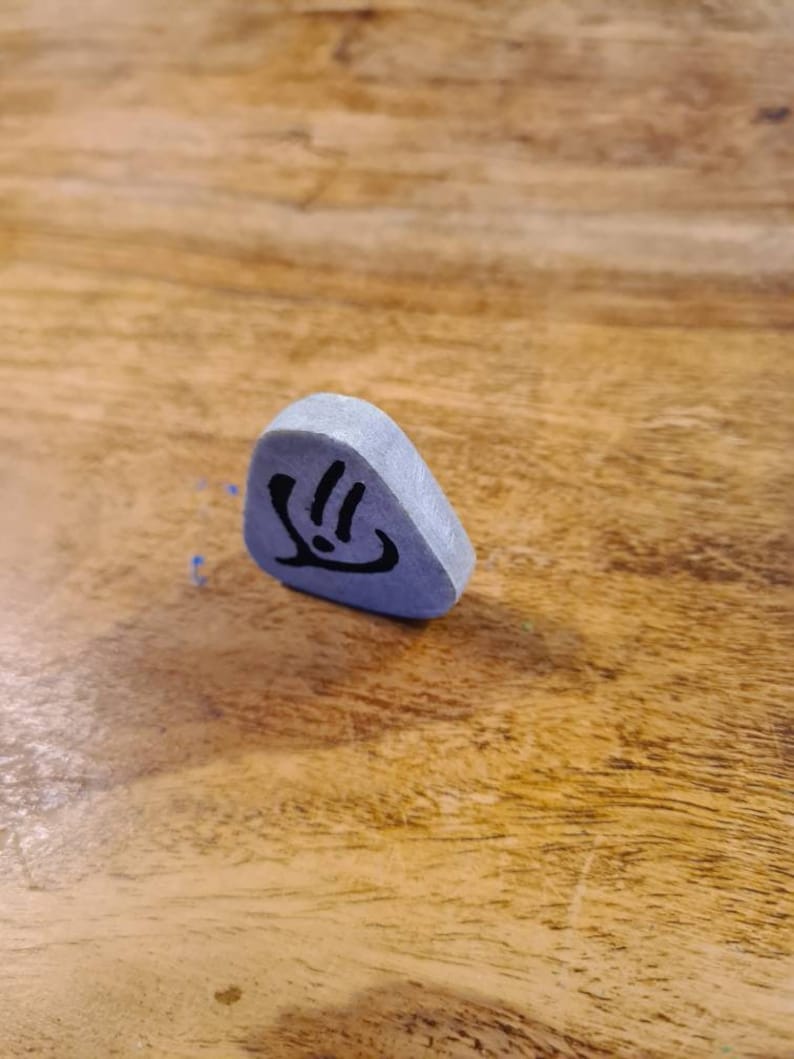 May include: A grey triangular-shaped stone with a black symbol on it. The symbol is a stylised hand with three fingers.