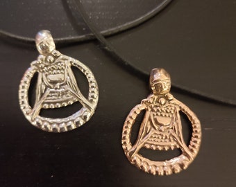 May include: Two silver and gold pendants with a detailed design of a woman holding a chalice. The pendants are on black cords.
