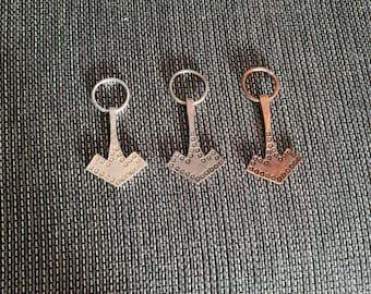 May include: Three metal keychains in the shape of a hammer with a ring at the top. The keychain on the left is silver, the middle keychain is silver, and the keychain on the right is copper.