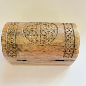 May include: A wooden chest with a carved Celtic knot design. The chest is rectangular with rounded sides and a hinged lid. The wood is light brown in colour. The chest is likely for storing small items.